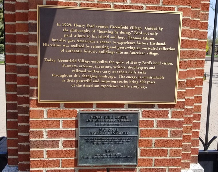The two plaques at the entrance to Greenfield. The top one reads, "In 1929, Henry Ford created Greenfield Village. Guided by the philosophy of 'learning by doing,' Ford not only paid tribute to his friend and hero, Thomas Edison, but also gave Americans a chance to experience history firsthand. His vision was realized by relocating and preserving an unrivaled collection of authentic historic buildings into an American village. "Today, Greenfield Village embodies the spirit of Henry Ford's bold vision. Farmers, artisans, inventors, writers, shopkeepers and railroad workers carry our their daily tasks throughout this changing landscape. The energy is unmistakeable as their powerful and inspiring stories bring 300 years of the American experience to life every day." The second reads, "Henry Ford Museum and Greenfield Village has been designated a National Historic Landmark. This site possesses national significance in commemorating the history of the United States of America. 1982. National Park Service. United States Department of the Interior."