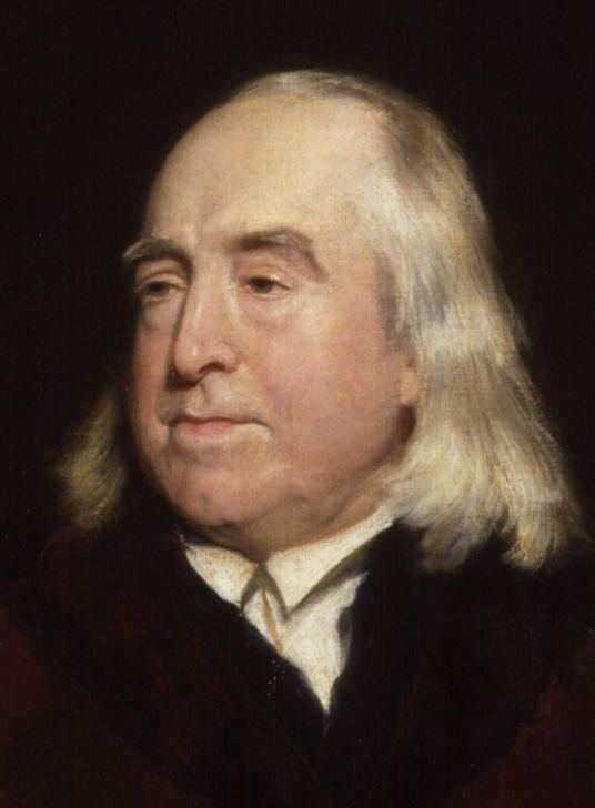 A painting of Jeremy Bentham, creator of the panopticon. Bentham is an older balding white man with an oval face, dark eyes, and white hair down to his shoulders.