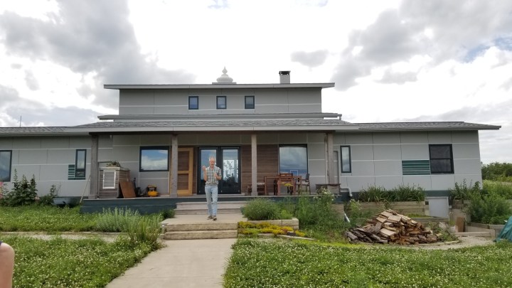 A low-lying very geometric gray building. A man stands in the garden in front of it.