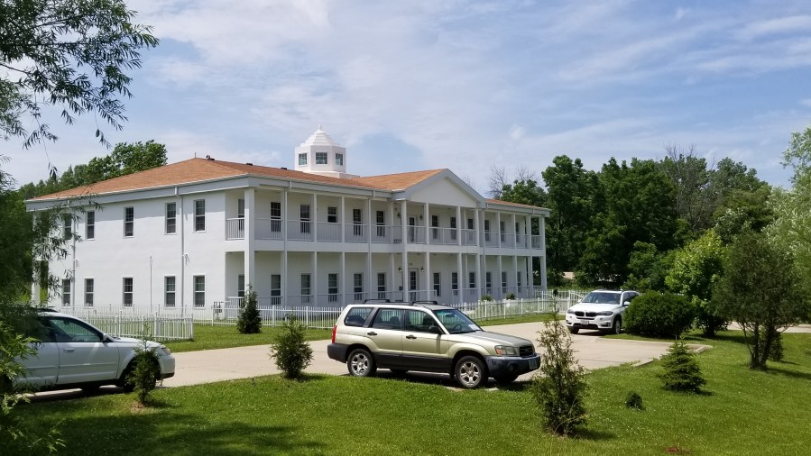 A white building with an orange roof. Windows are arrayed along the front, and a small tower is set in the center of the roof.