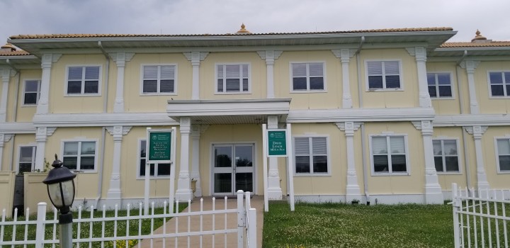 The entrance to a yellow and white building with two green signs out front.