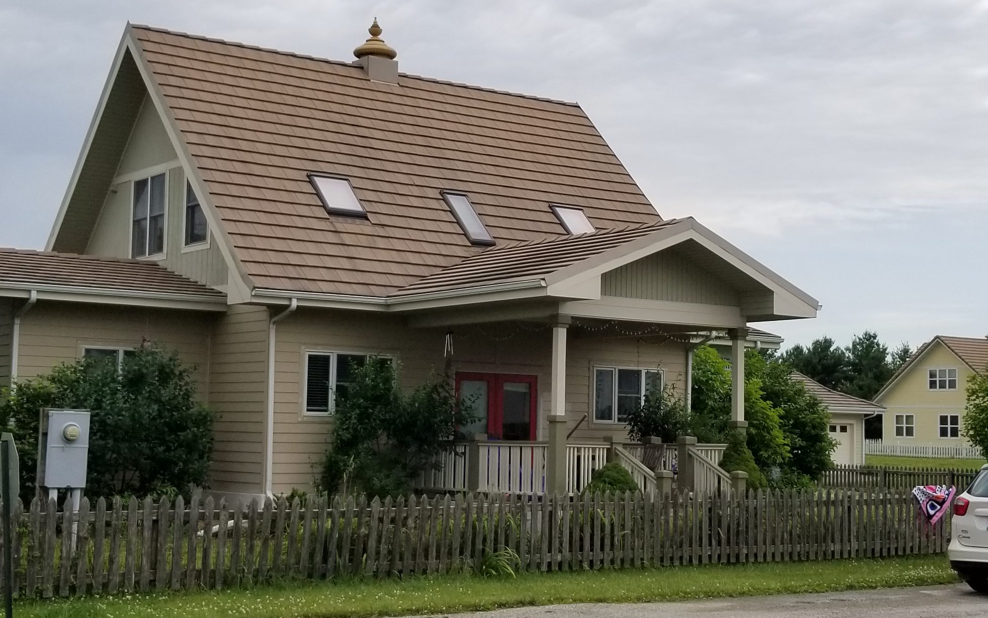 A traditional single family home, featuring a small roof ornament and a surrounding wooden fence.
