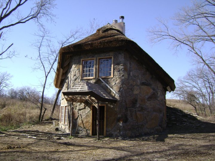 A small, hexagonal stone house with a single window and a thatch roof.